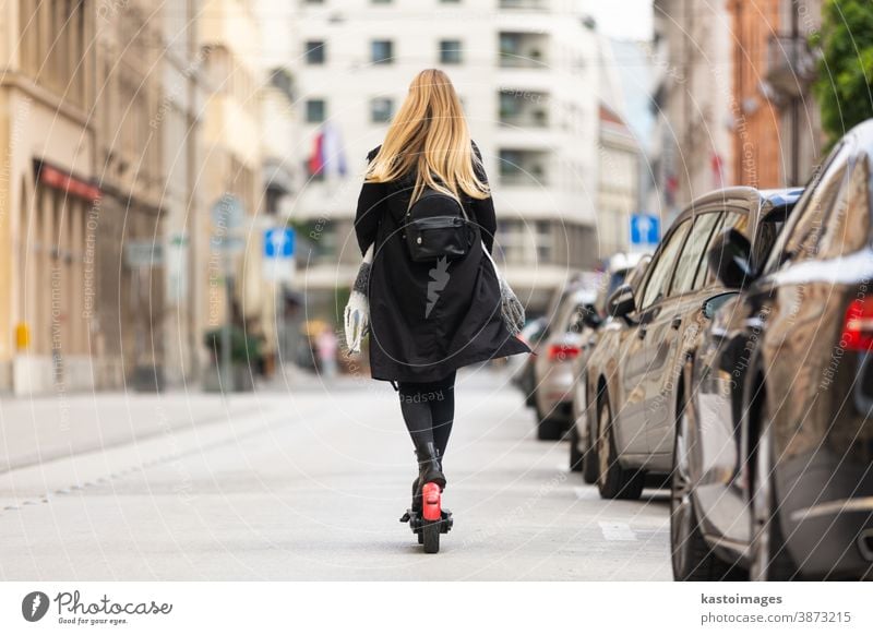 Rear view of girl riding public rental electric scooter in urban city environment. New eco-friendly modern public city transport in Ljubljana ride e-scooter