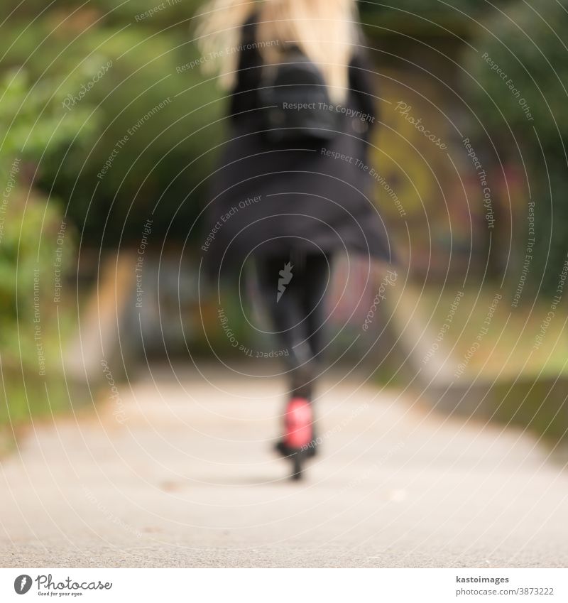 Out of focus rear view of casual caucasian teenager riding urban electric scooter in city park during covid pandemic. Urban mobility concept. transport woman