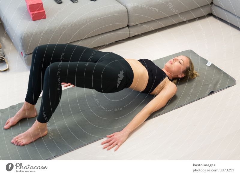 Beautiful blonde woman doing home workout indoors. Woman practice yoga at home. Fit girl using workout tutorials for healthy active lifestyle. Woman using quarantine for home workouts.