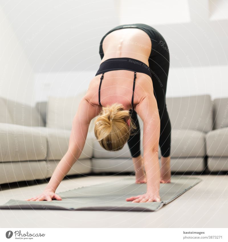 Beautiful blonde woman doing home workout indoors. Woman practice yoga at home. Fit girl using workout tutorials for healthy active lifestyle. Woman using quarantine for home workouts.