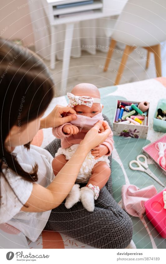 Girl trying on her doll a mask that she is sewing girl adjusting mask putting on mask baby doll cloth mask sewing box covid-19 hand made protection care