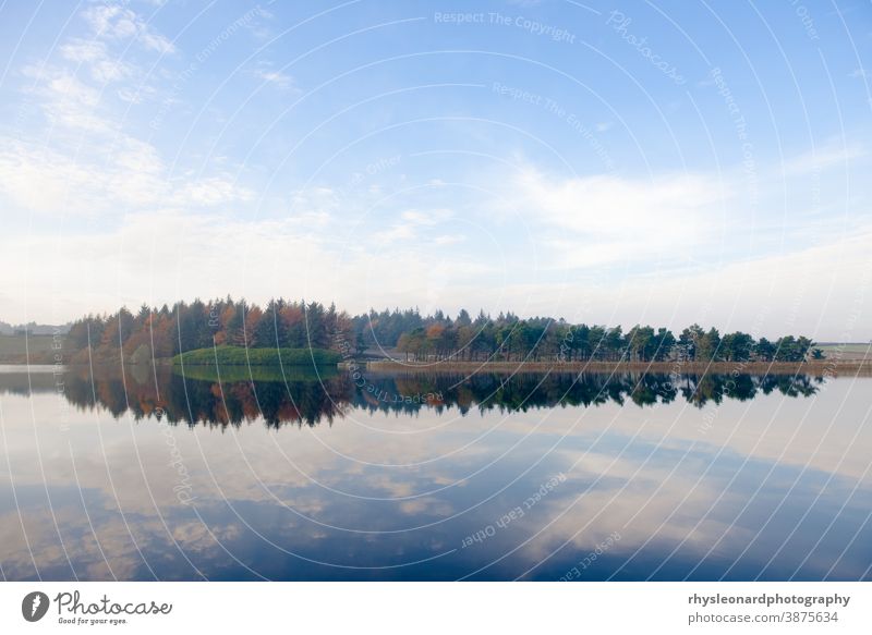 Stunning blue skies reflected in mirror like redmires reservoir water Forest conifers autumn texture landscape Reflection trees ripples hazy reservoirs