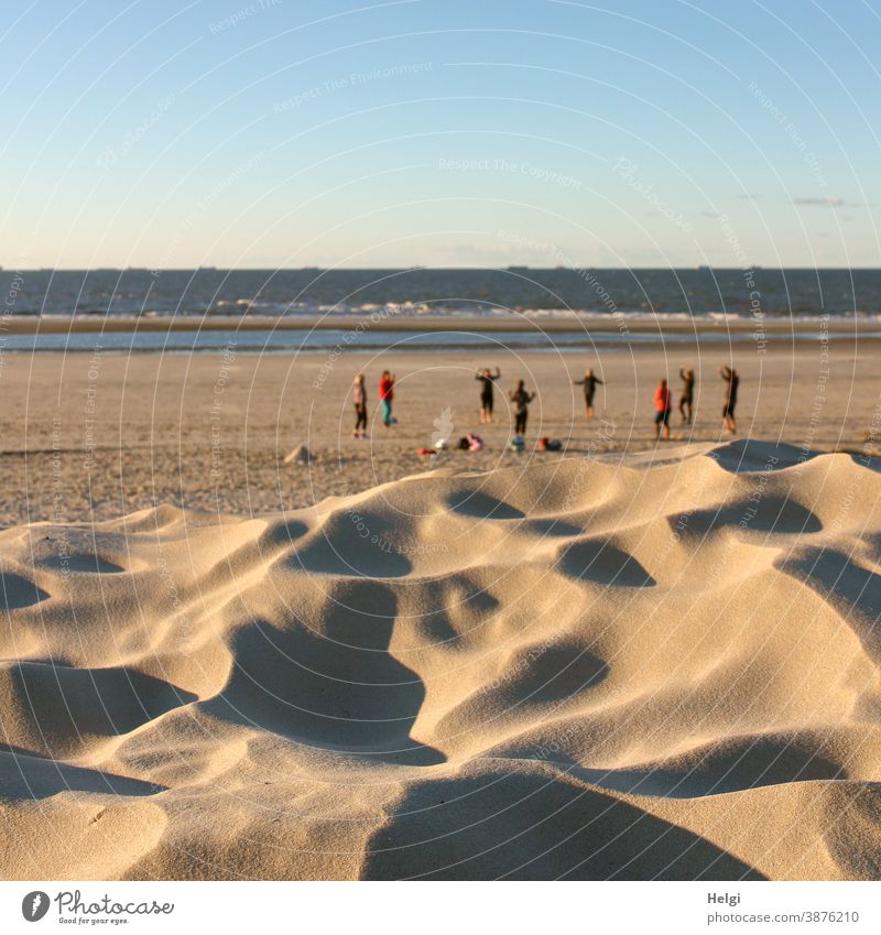 sporty - behind a sand dune a gymnastics group is doing gymnastics on the beach of the North Sea Sand Beach duene North Sea beach Gymnastics group Sports