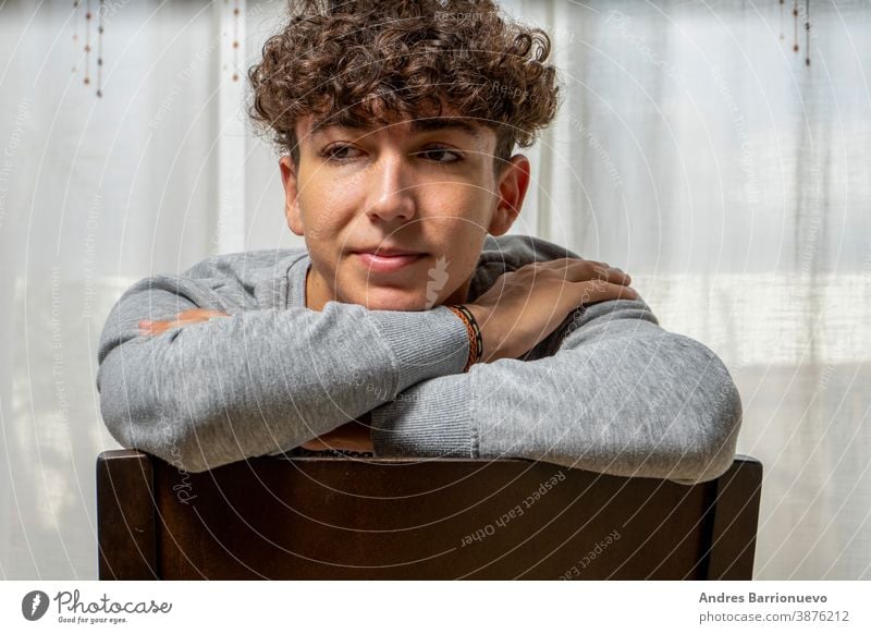 Attractive young man with curly hair wearing gray sweatshirt posing on white curtains background cheerful casual smile male adult handsome happy attractive