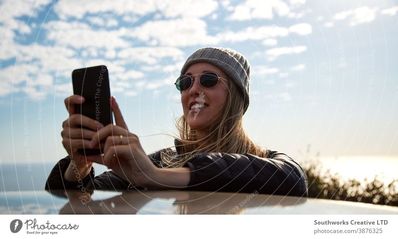 Young Woman On Road Trip Vacation Leaning On Roof Of Rental Car Using Mobile Phone road trip taking photo woman young women holiday vacation car driving driver