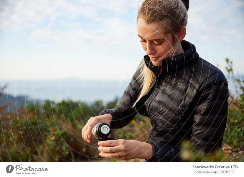 Young Woman Taking A Break From Countryside Hike And Pouring Coffee From Flask hike walking woman young women hiking trek camping taking a break pouring drink