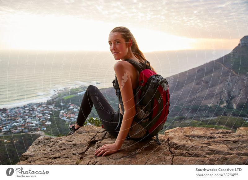 Portrait Of Young Woman Hiking Along Coastal Path Watching Sun Setting Over Sea sunset sunrise golden hour happy woman young women hike hiking walk walking trek