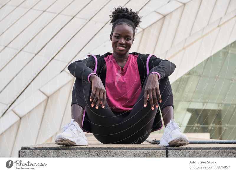 Serious black sportswoman sitting on stone border in city athlete determine confident runner street serious fit sportswear female ethnic african american