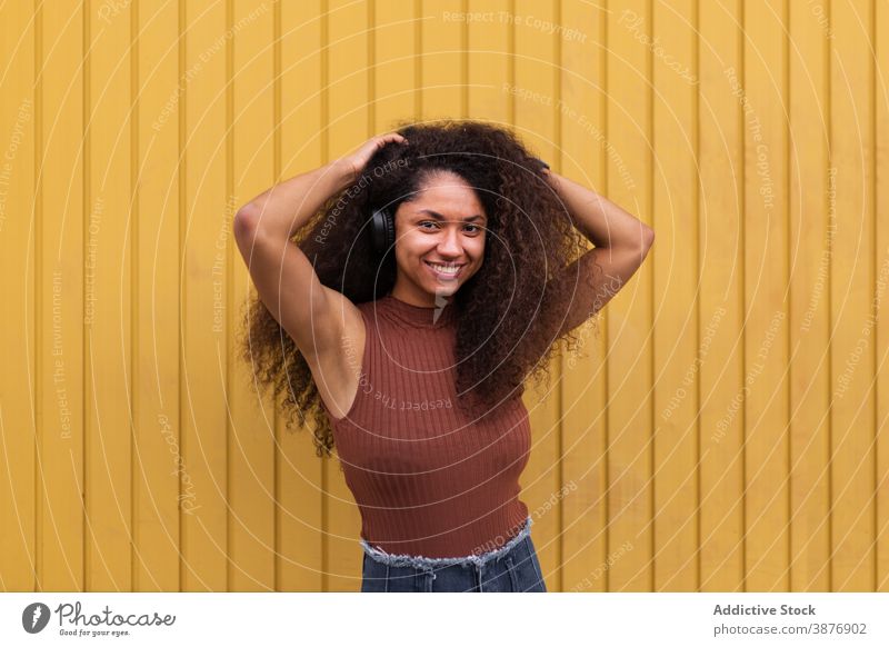 Charming ethnic woman with headphones on street curly hair afro hairstyle charming smile natural beauty female listen black african american city trendy rest