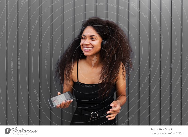 Optimistic black woman listening to music on street headphones meloman enjoy afro hairstyle curly hair smartphone female ethnic african american city sound