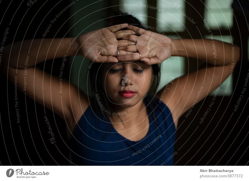 An young and attractive Indian Bengali brunette woman in active wear is doing yoga after waking up in the morning in front of window in her room. Indian lifestyle.