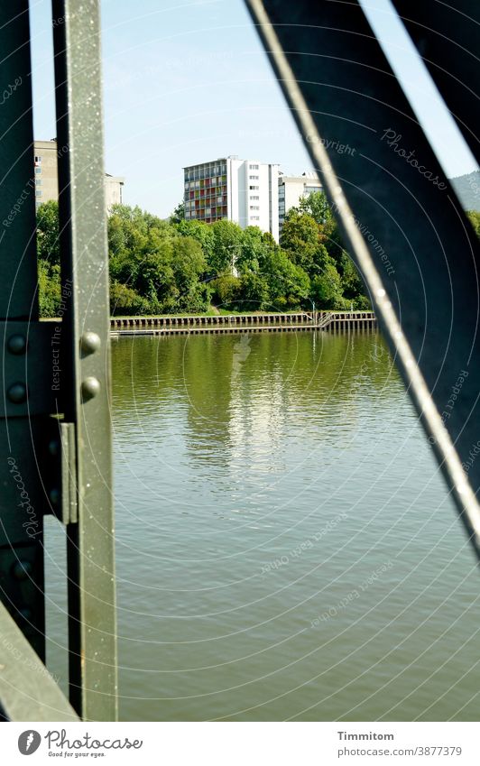 What is this picture trying to tell us? Heidelberg Neckar Bridge Steel bridge houses blocks of flats bushes Water Sky Bank reinforcement Stud Steel construction