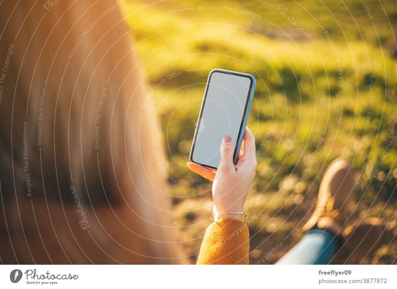 Mockup of a woman with her phone mockup white screen technology communication internet nature mock up copy space yellow coat autumn winter unrecognizable boots