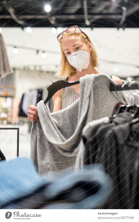 Fashionable woman wearing protective face mask shopping clothes in reopen retail shopping store. New normal lifestyle during corona virus pandemic coronavirus