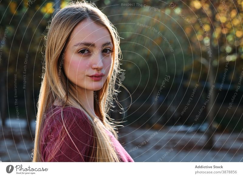 Long haired young woman looking at camera in park long hair blond confident modern autumn portrait natural teen female style teenage millennial fair hair lady