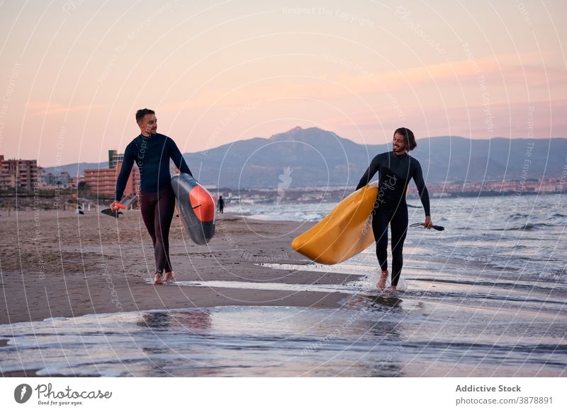 Men with paddleboards walking along beach surfer men surfboard sea sunset male friend friendship seashore nature wet summer seaside water coast cheerful