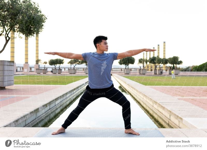 Man doing yoga in Warrior pose man warrior pose flexible practice virabhadrasana barefoot mat city stretch male ethnic asian mindfulness vitality harmony