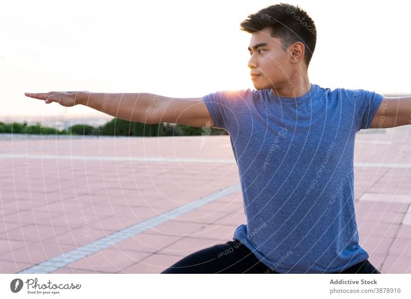 Ethnic man in sportswear doing yoga at sunset warrior pose practice asana flexible focus tranquil male ethnic asian virabhadrasana urban park mat healthy