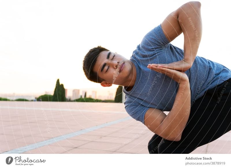 Peaceful man in Revolved Chair pose practicing yoga at sunset revolved chair pose flexible practice peaceful harmony yogi male ethnic asian sundown asana serene