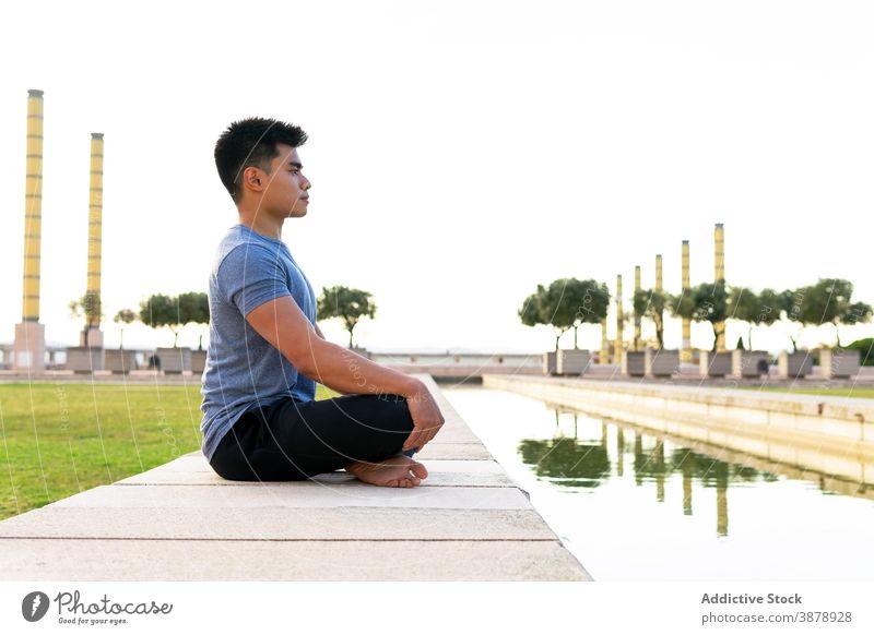 Tranquil man mediating in Lotus pose in park lotus pose meditate yoga harmony asana padmasana flexible legs crossed practice male ethnic asian mat relax calm