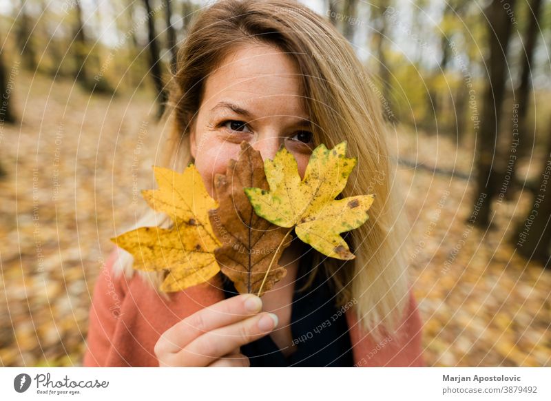 Young woman holding yellow autumn leaves in the forest 30s adult beautiful beauty blonde caucasian cheerful color cute enjoy fall female foliage fresh fun girl