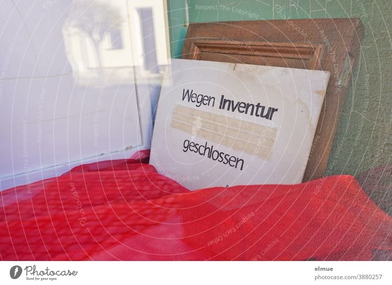 "Closed for inventory" is written on a cardboard sign leaning against the wall in the empty shop window display covered with red cloth Inventory