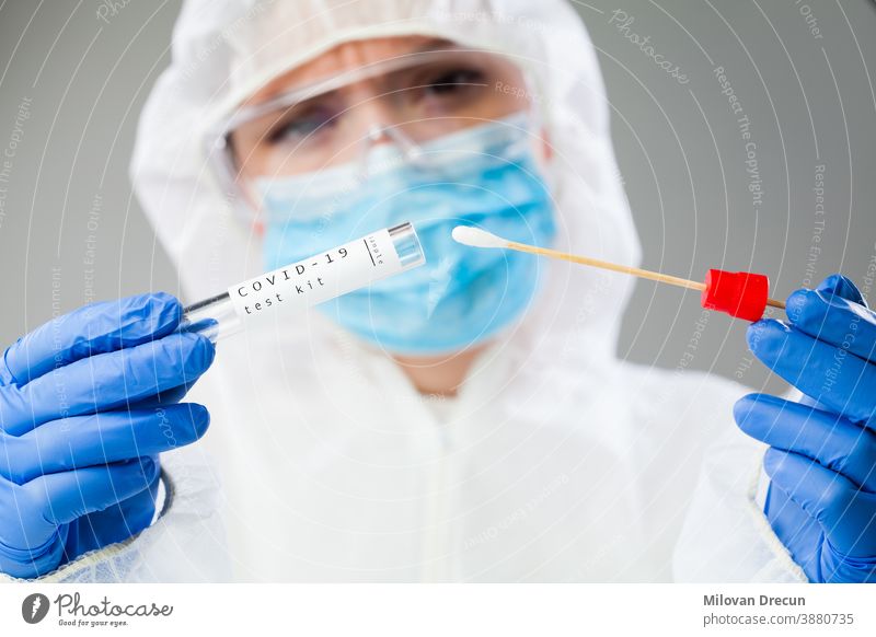 Female doctor in coveralls holding COVID-19 PCR nasal swabbing kit analysis analyzing care clinic contamination corona coronavirus covid covid19 diagnostic