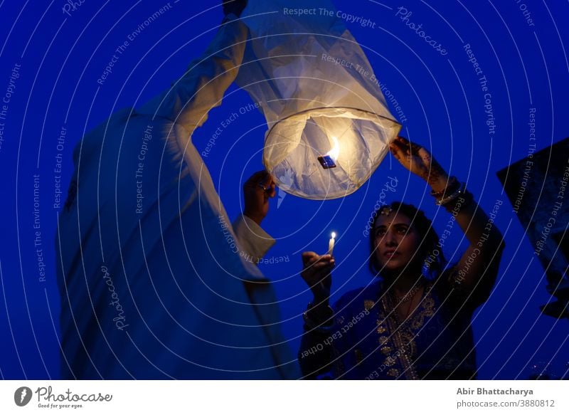 An Indian Bengali couple is celebrating Diwali by lighting flying lanterns in the sky in blue hour. Indian lifestyle and Diwali celebration action active adult