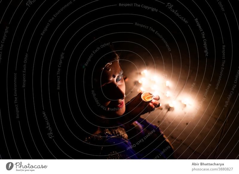 Young and beautiful Indian Gujarati woman in Indian traditional dress celebrating Diwali with illuminated diya/lamps on rooftop on Diwali evening. Indian lifestyle and Diwali celebration