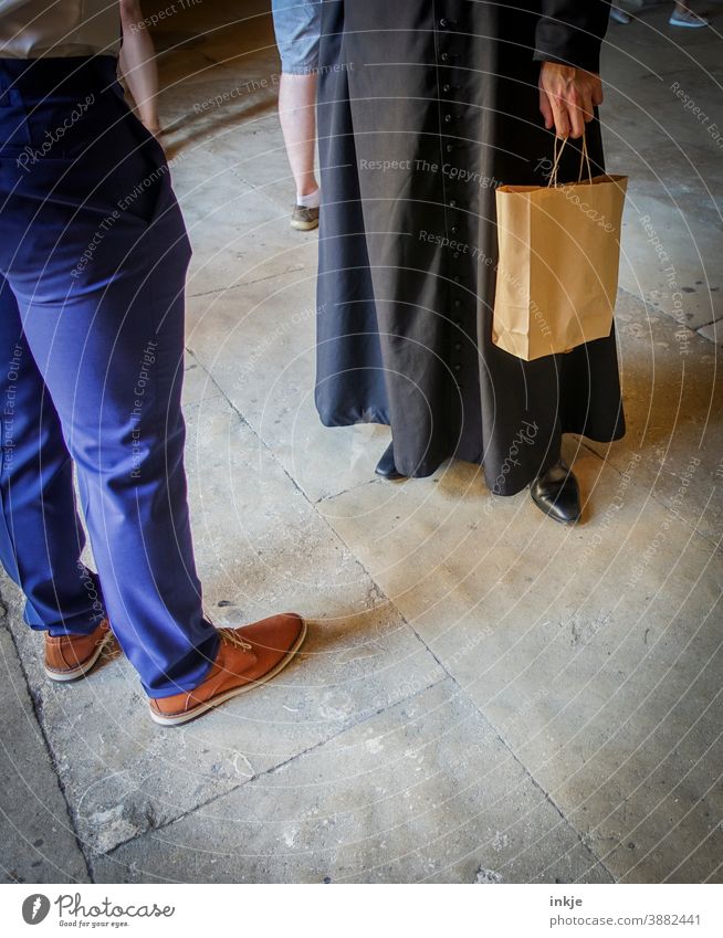 Man in gown with paper bag and man in cloth pants face each other Colour photo people Opposite Stand Robe Pants Footwear conversation communication Clergyman