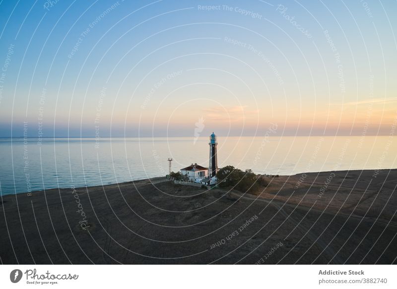 Lonely lighthouse on coast of sea at sunset beacon navigate tower sky twilight landscape amazing calm hill ocean picturesque shore sundown peaceful scenic