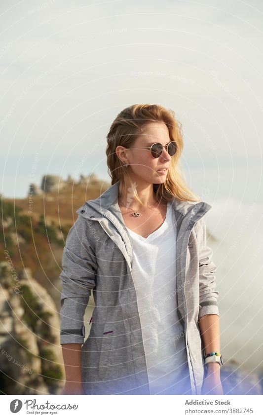 Woman in sunglasses standing on hill in summer hiker woman traveler carefree adventure wanderlust sunny mountain terrain female rock area trekking vacation