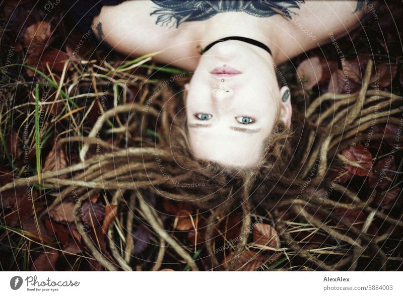 Portrait of a young woman with dreadlocks and tattoos on the forest floor in autumn Woman Dirty Blonde tattooing Jewellery Piercing earring Concealed Direct