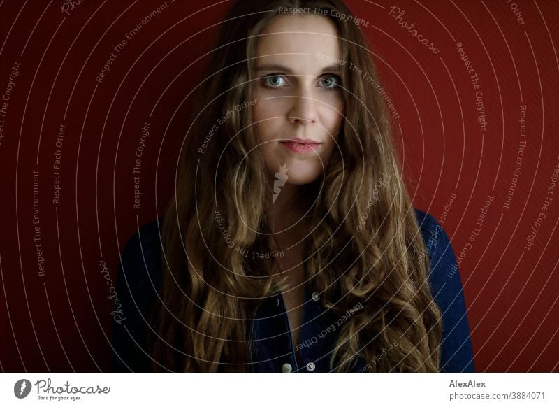 Portrait of a young woman in front of a red wall Woman Slim pretty Brunette long hairs Face smart emotionally see look Looking Direct naturally Fair-skinned