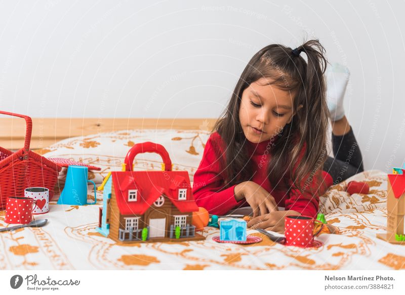 Cute little girl in red long neck t-shirt sweater playing with her toys in the bedroom. holiday christmas childhood hispanic latin home merry portrait isolated