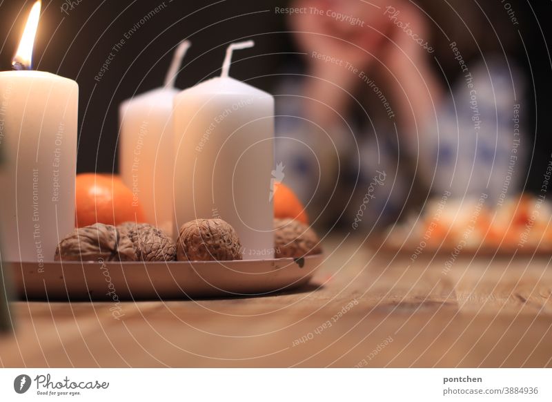 A child is sitting at the dining table in front of an Advent wreath with a burning candle. First Advent, Tradition, Christmas Christmas wreath Anticipation