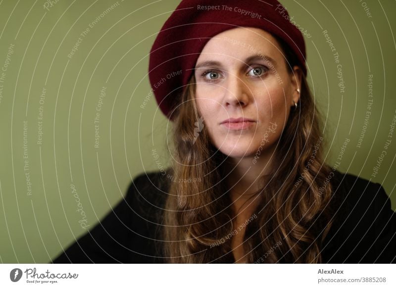 Portrait of a young woman with hat in front of a green wall Woman Slim pretty Brunette long hairs Face smart emotionally see look Looking Direct naturally