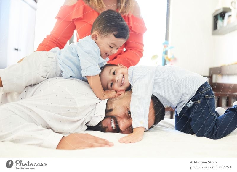 Cheerful ethnic family on bed at home gather having fun pastime together couple son sibling hispanic relationship love fondness kid child cuddle affection enjoy