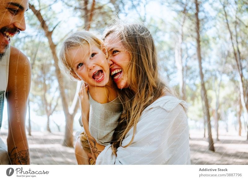 Mother and father cuddling kid together family cheek child love mother cuddle unity multiethnic multiracial diverse forest hug tender daughter parent happy