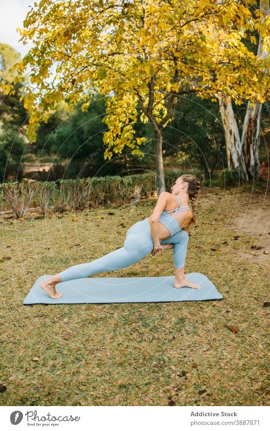 Young woman doing twisted standing yoga pose park bound revolved crescent lunge parivrtta baddha anjaneyasana stretch practice female wellness lifestyle harmony