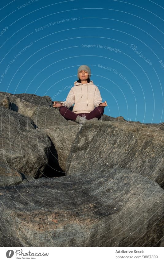 Focused woman meditating on rock meditate yoga lotus pose mudra relax stone blue sky nature mindfulness zen female asana padmasana practice wellness harmony