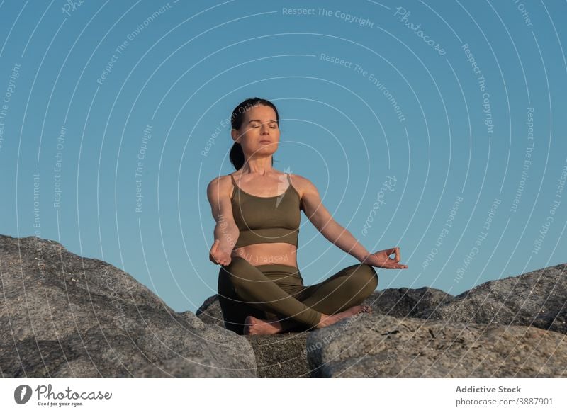 Relaxed woman meditating in nature meditate yoga lotus pose mudra relax stone rock mindfulness zen female asana padmasana practice wellness harmony wellbeing