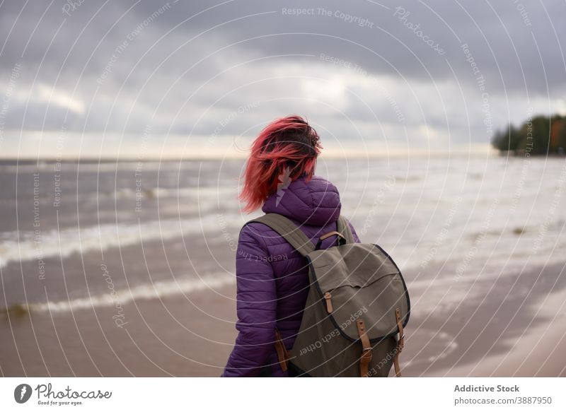 Anonymous female backpacker relaxing on sandy beach alone autumn sea travel woman solitude admire gloomy stand sestroretsk saint petersburg russia