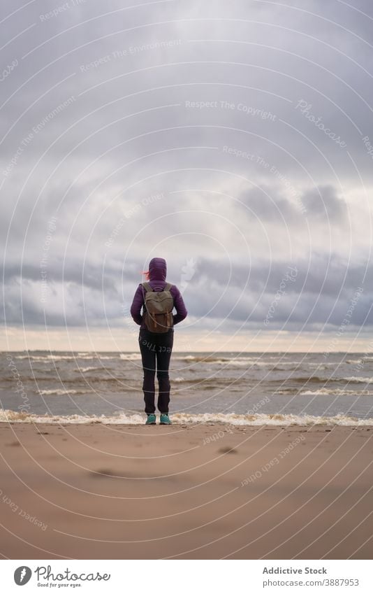 Anonymous female backpacker relaxing on sandy beach alone autumn sea travel woman solitude admire gloomy stand sestroretsk saint petersburg russia