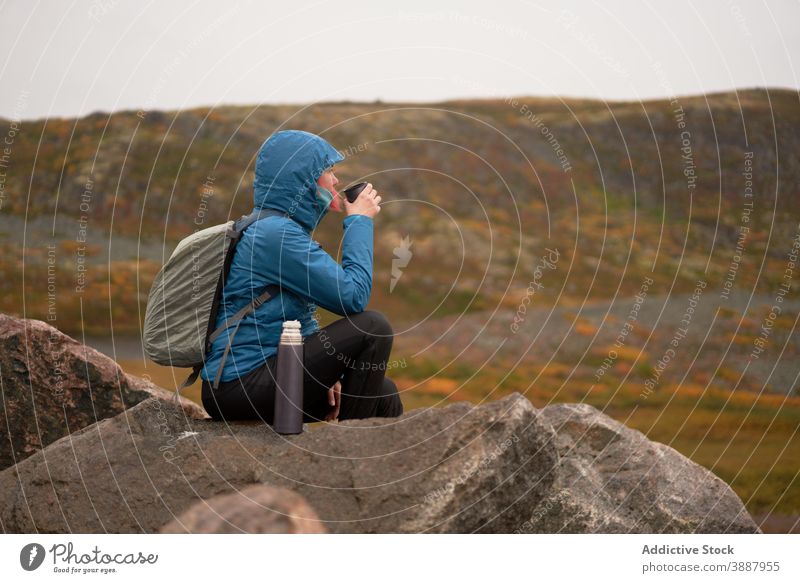 Female explorer drinking tea from thermos cup in highlands traveler woman mountain hot autumn gloomy adventure female wanderlust landscape rock outerwear