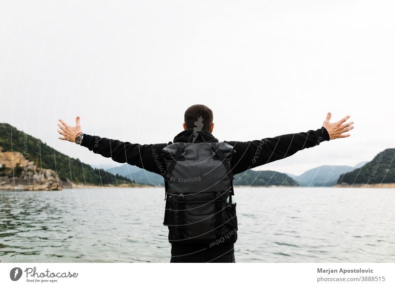 Young male nature explorer enjoying the view of the mountain lake adventure autumn backpack beach blue cliff countryside day forest freedom guy hands hike hiker