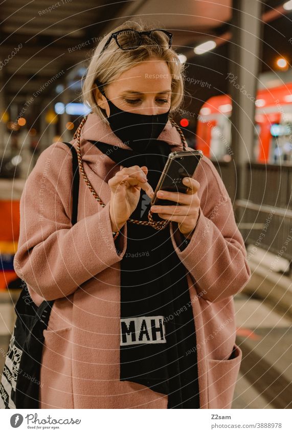 Young woman standing at the station with a corona mask coronavirus Blonde long hairs Track voyage Company Winter Coat Eyeglasses Fashion style Looking pretty