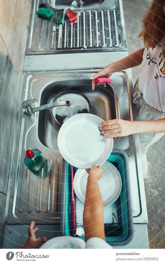 Teenager girl washing up the dishes pots and plates with help her younger sister in the outdoor kitchen during vacations on camping working together siblings