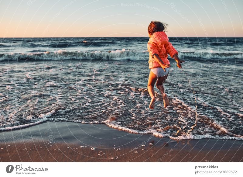 Playful little girl jumping over sea waves on a sand beach at sunset excited free enjoy positive emotion carefree nature outdoors travel happiness happy summer