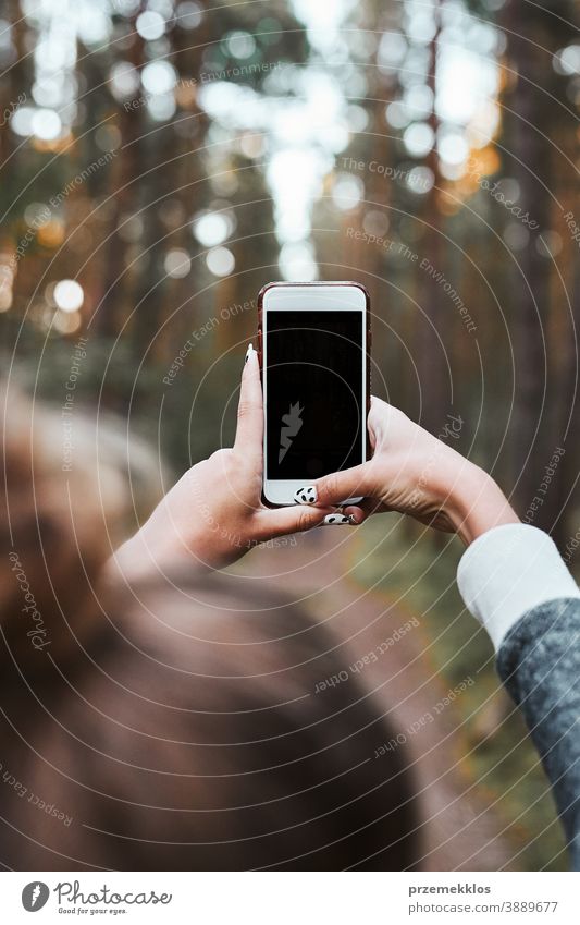 Young woman taking photos using smartphone during walk in a forest on summer vacation trip active activity destination enjoy exploration female hike lifestyle